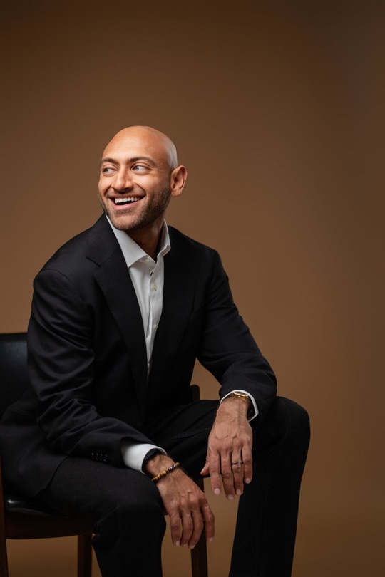 Gabriel Alizaidy in a black blazer and white shirt, seated and smiling